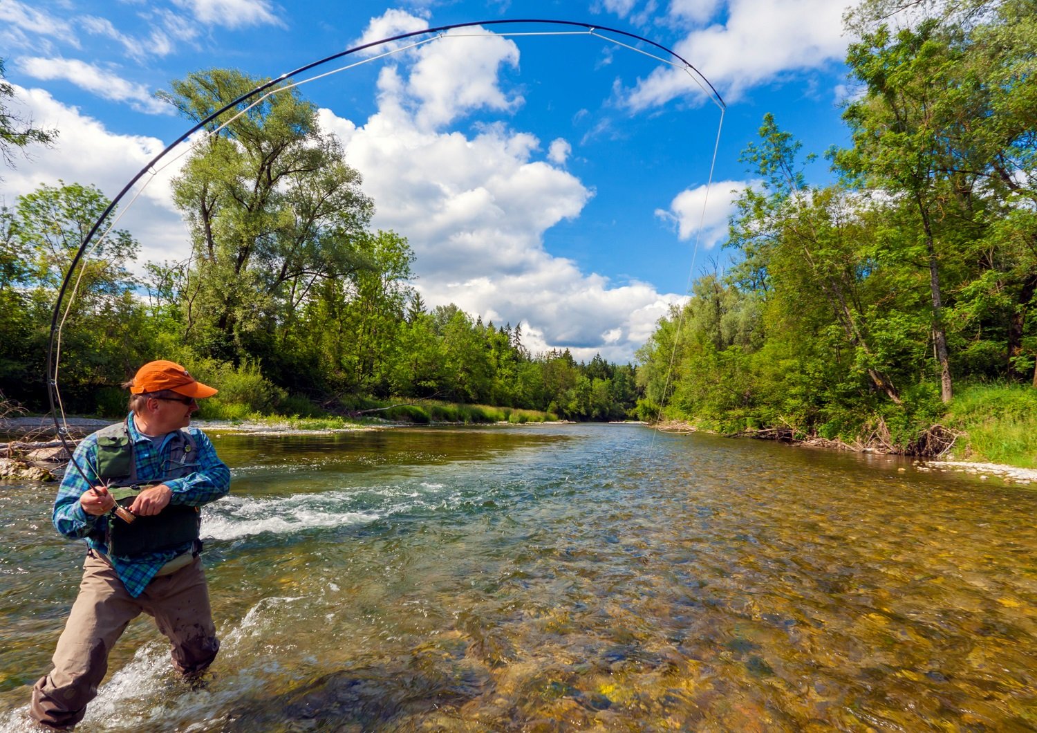 A fisherman is flyfishing in a beautiful River on a perfect Day.